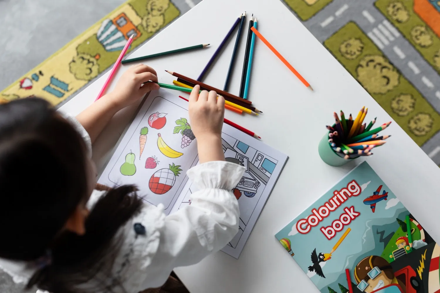 A child drawing with coloured pencils beside picture books