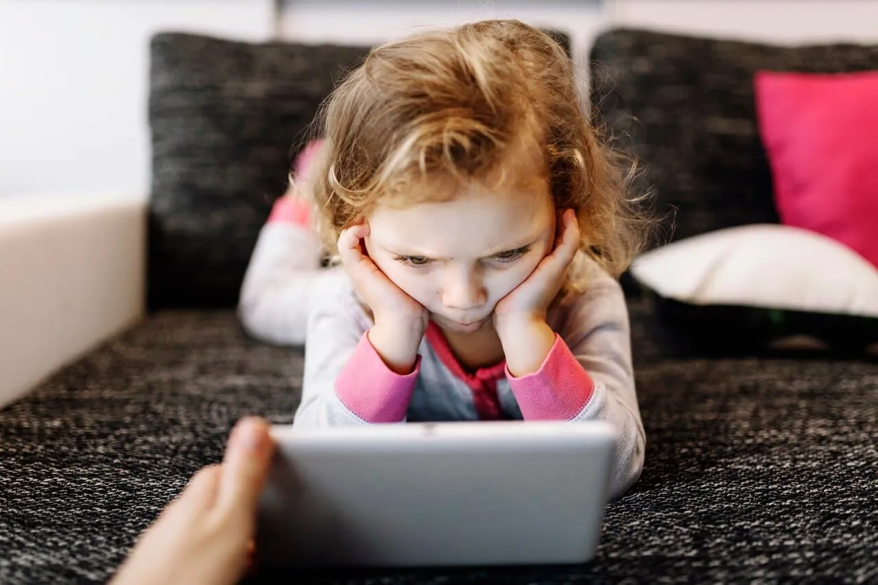 A child looking at a tablet with her head resting in her hands