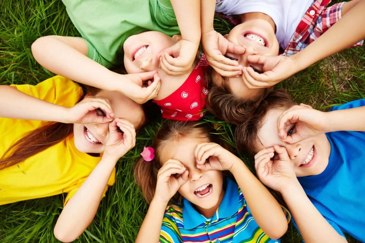 Children lying in a circle on grass and smiling