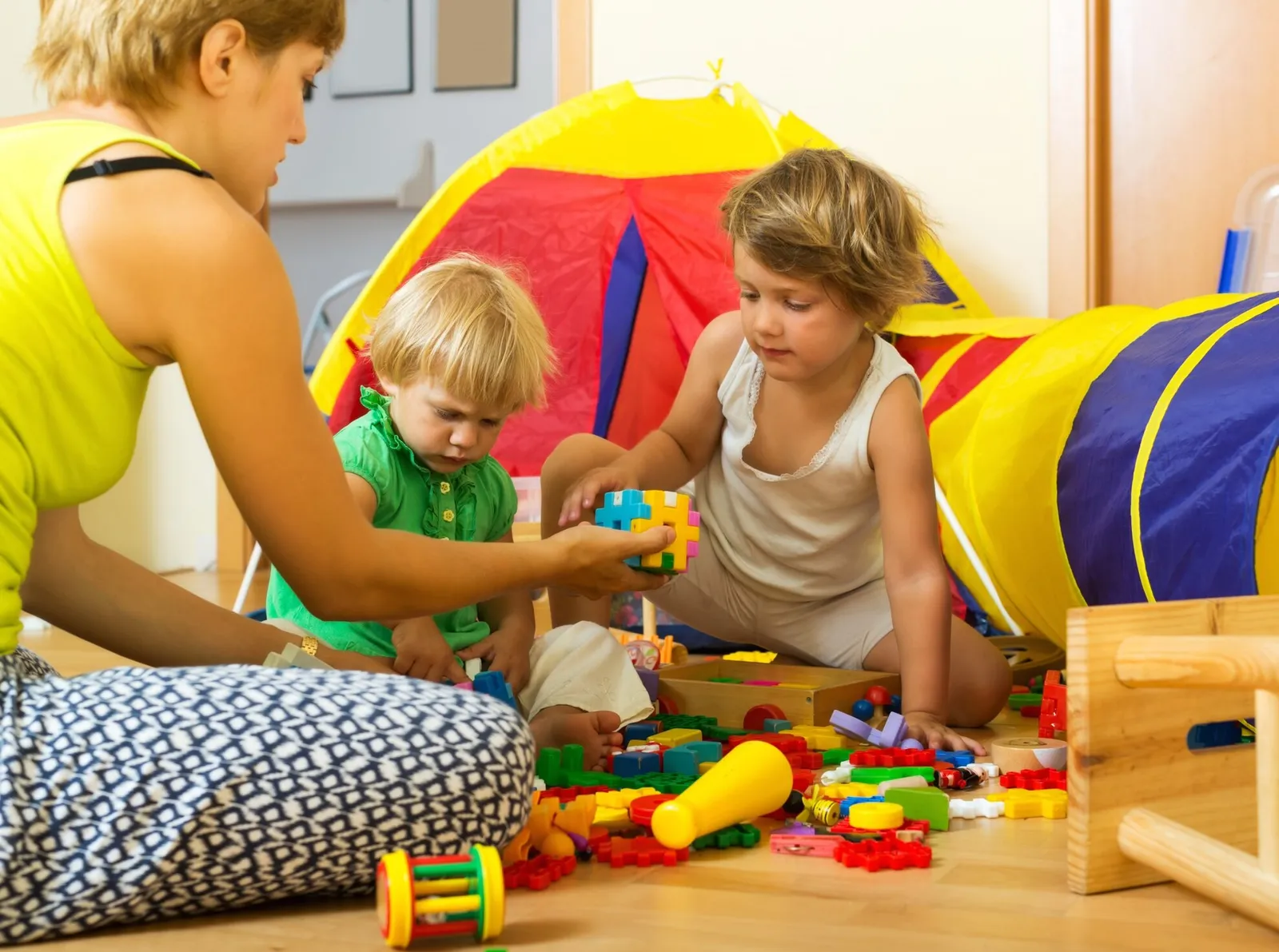 A caregiver and children playing with toys beside a play tent