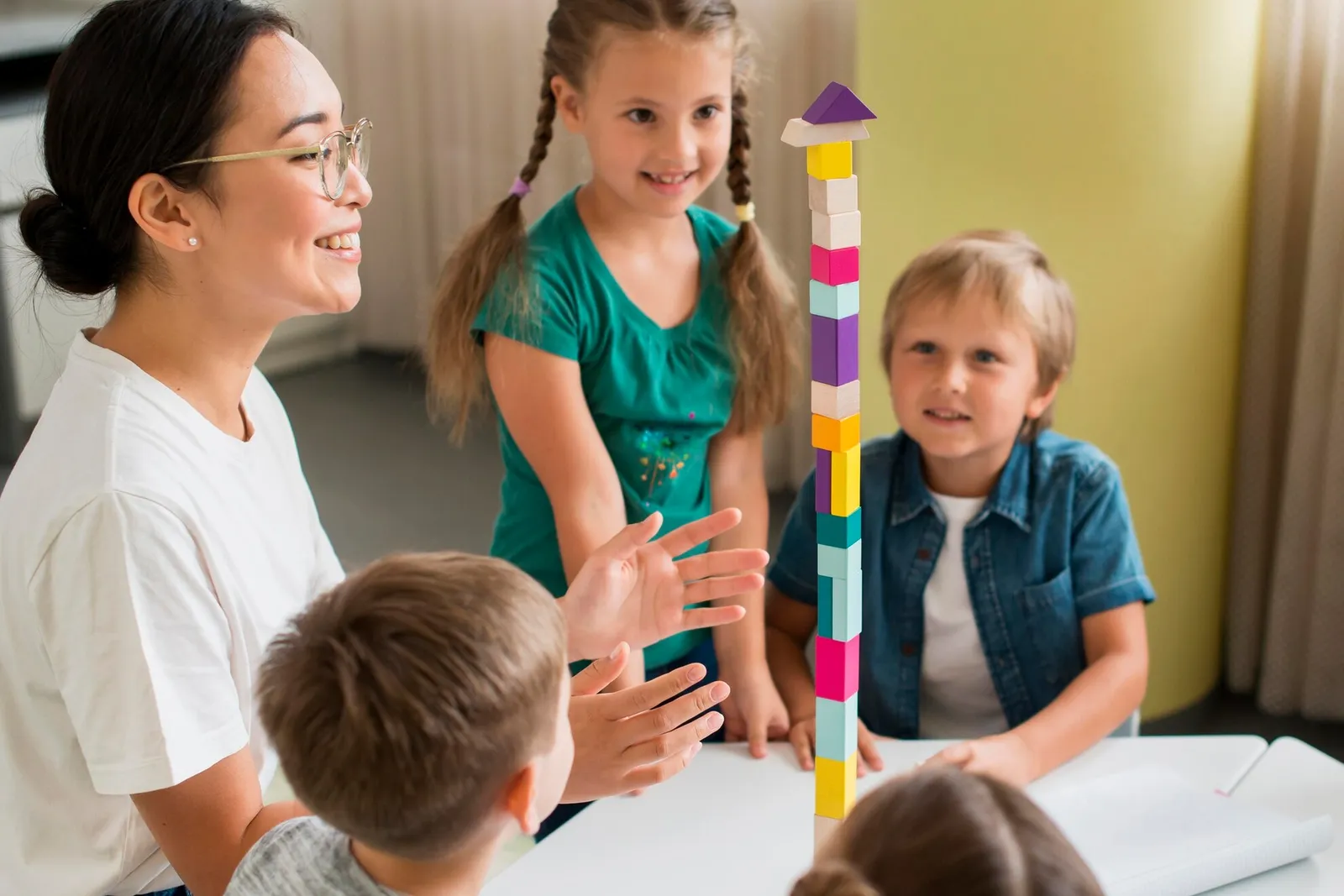 A teacher and preschoolers building a colourful block tower