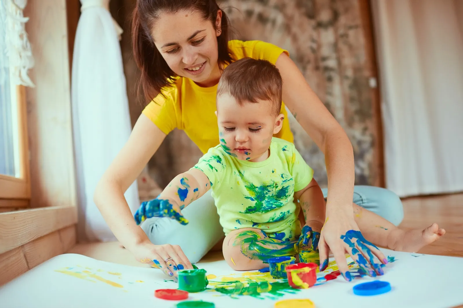 An adult helping a toddler paint with bright colours
